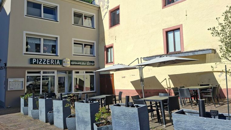 A pizzeria with an outdoor area on a charming street. Tables and chairs are set up under umbrellas.