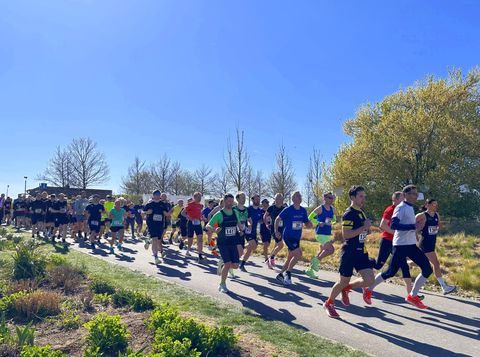 Un groupe de coureurs participe à une course dans un parc ensoleillé. L'ambiance est animée et les participants portent des vêtements de sport.