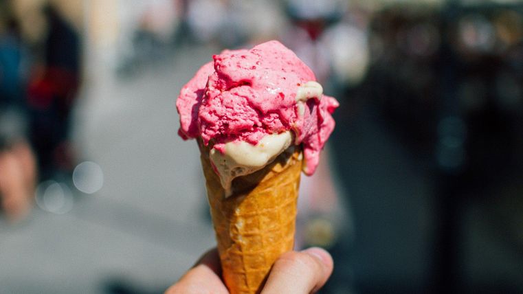 Eine Hand, die eine Eiswaffel mit einer rosafarbenen und einer beigefarbenen Kugel Eis hält.