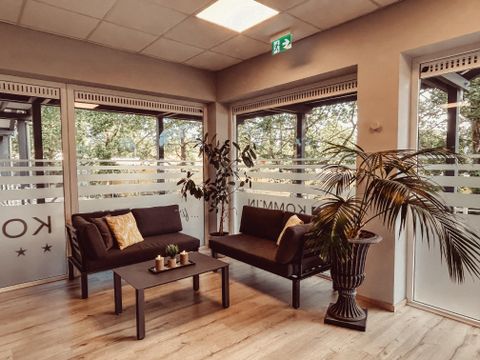 Une salle d'attente moderne avec deux canapés et une table. De grandes fenêtres offrent une vue sur la nature et laissent entrer beaucoup de lumière.