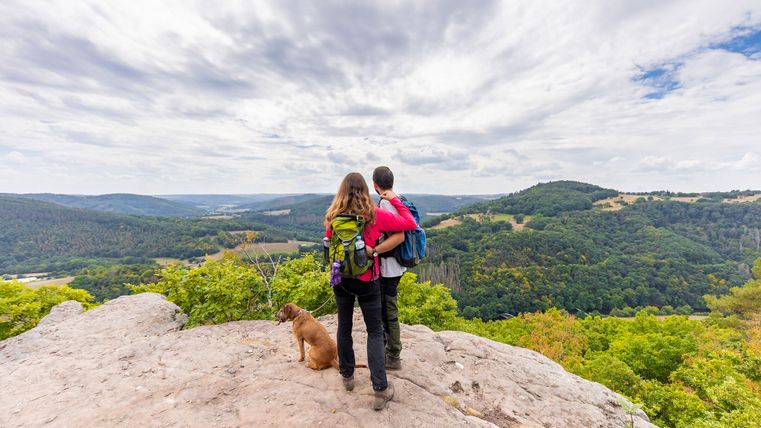 Ein Paar steht mit einem Hund auf dem Eugenienstein und genießt die Aussicht