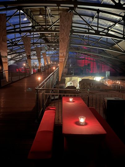 Ein stilvolles Restaurant mit einer modernen Glasdecke und warmem Licht. Rote Tische und Kerzen schaffen eine gemütliche Atmosphäre.
