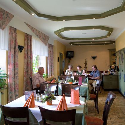 Een gezellig restaurant met gedekte tafels en een uitnodigende sfeer. Enkele gasten zitten samen en genieten van hun tijd.