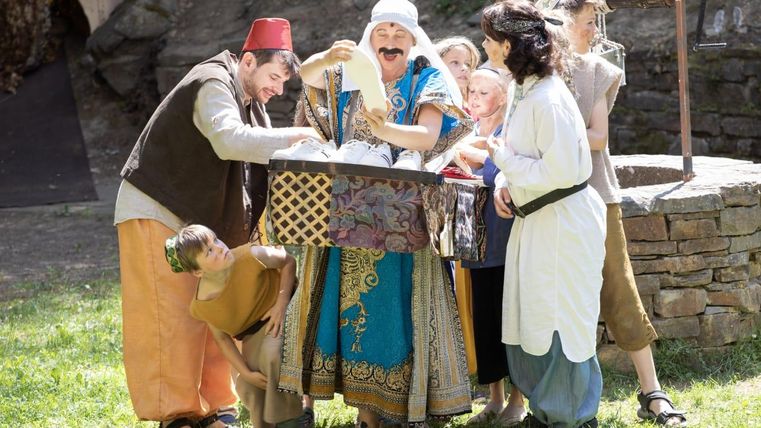 Een groep kinderen en volwassenen in historische kostuums verzamelt zich rond een tafel. Ze lijken plezier te hebben en samen iets te beleven.