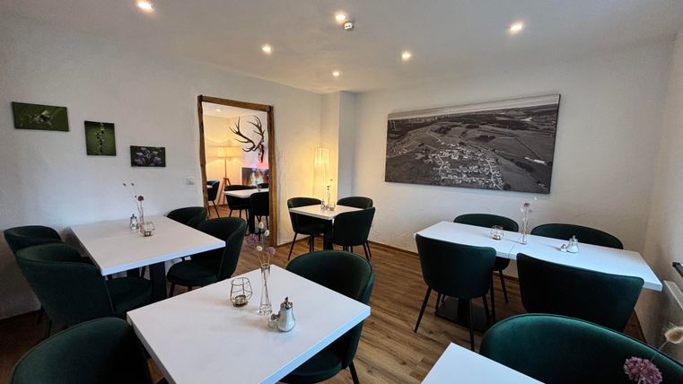 A modern restaurant with bright walls and elegant, round tables. The chairs are green and a large wall art adorns the space.