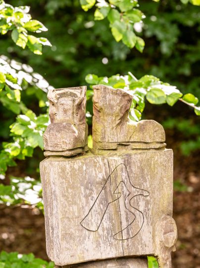 Houten blok met een hoofdletter A en een hoofdletter S voor AhrSteig daarboven staan twee gebeeldhouwde wandelschoenen 