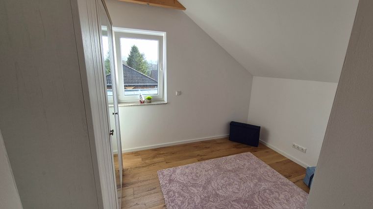 Une pièce lumineuse avec une fenêtre et un tapis confortable. Sur le sol en bois, se trouvent quelques meubles, y compris un sac.