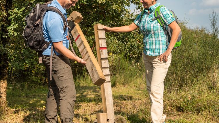 Twee wandelaars kijken naar een houten stoeprand op een wandelpad.
