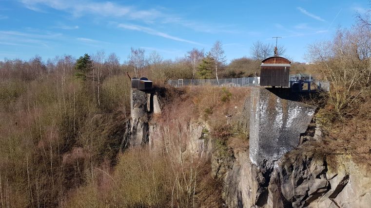 An impressive cliff with a lookout point and a small cottage at the top. Surrounded by trees and a clear sky.