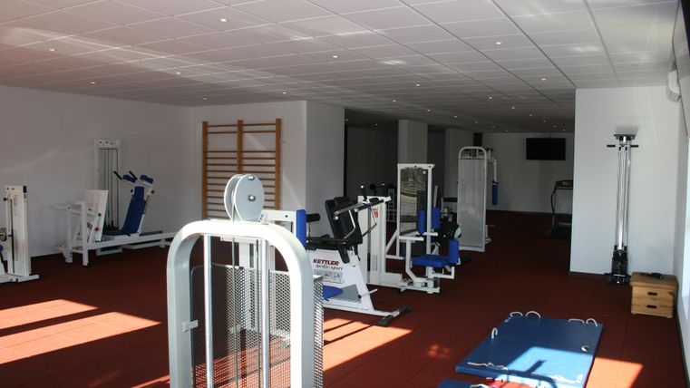 A modern gym with various workout equipment. The room is well-lit and has a plain, clean floor.