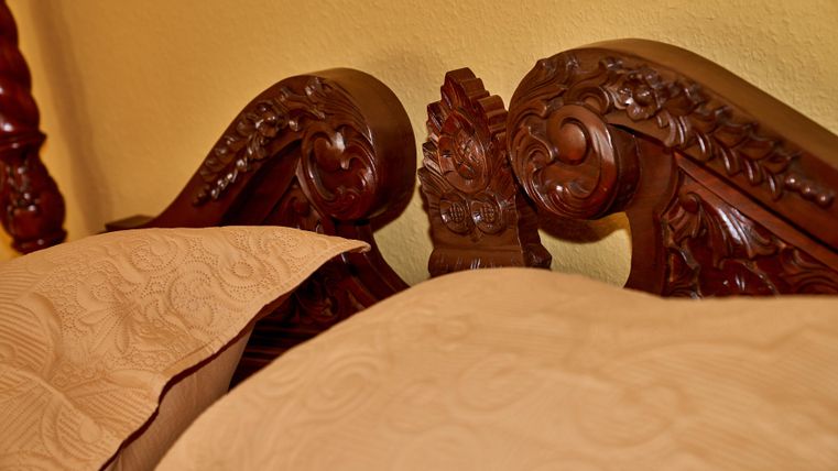Ein kunstvoll geschnitztes Kopfteil aus Holz mit eleganten Details. Dazu liegen zwei helle Kissen auf einem Bett.