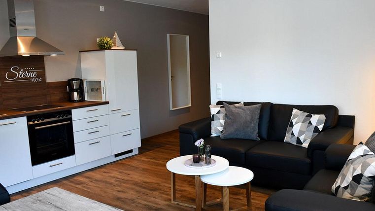 Un appartement moderne avec une cuisine ouverte et un coin salon confortable. Les meubles sont dans des couleurs neutres, avec deux petites tables au centre.