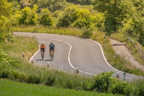 Zwei Radfahrer auf einer kurvigen Landstraße in der Eifel.