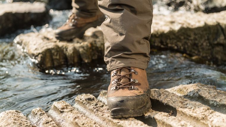 Close-up van een wandelschoen op een rots boven een stromend beekje.