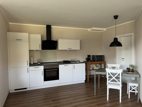 Une cuisine moderne avec des meubles blancs et une table à manger. Des appareils de cuisine comme une cuisinière et un micro-ondes sont visibles.