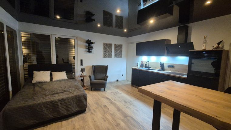 A modern room with a bed and a cozy armchair. The kitchen is open and well-equipped.