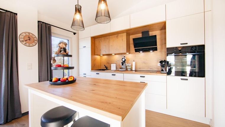 Moderne keuken met een houten eiland en elegante stoelen. Heldere verlichting en decoratieve elementen creëren een uitnodigende sfeer.