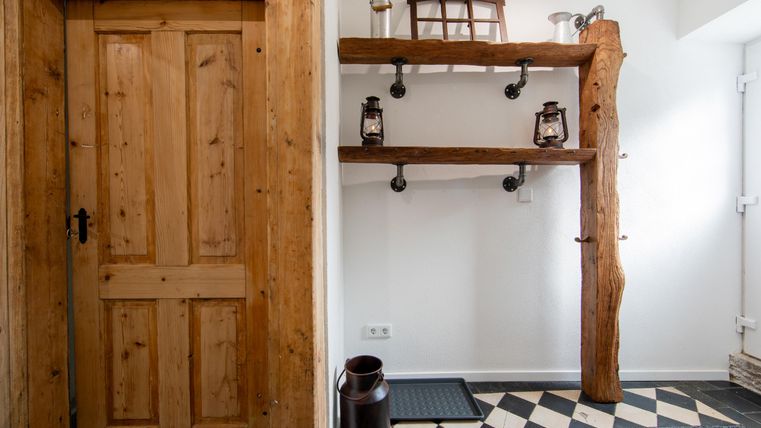 Ein einladender Eingangsbereich mit einer Holzplatte und einer rustikalen Tür. Der Boden hat ein schwarz-weißes Muster und es gibt dekorative Laternen.