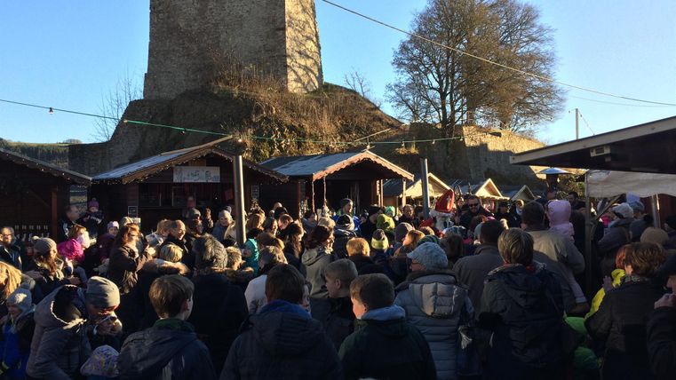 Une grande foule se rassemble sur un marché devant une ancienne tour. Il y a de nombreux stands et une ambiance festive.