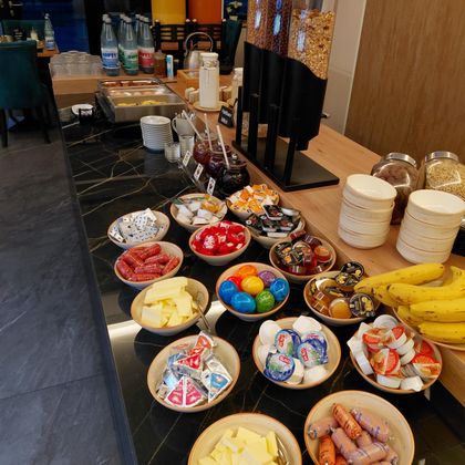 Un buffet avec différents ingrédients pour le petit-déjeuner. Il y a de la charcuterie, du fromage, des fruits et des sucreries ainsi que des boissons.