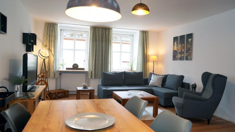 A cozy living room with a modern sofa and a dining area. Large windows let in plenty of daylight and give the room an inviting atmosphere.