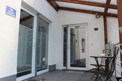 Un hall d'entrée accueillant d'une maison de vacances avec une porte en verre et un auvent en bois. À une petite table, deux chaises sont installées, idéales pour un moment de détente.