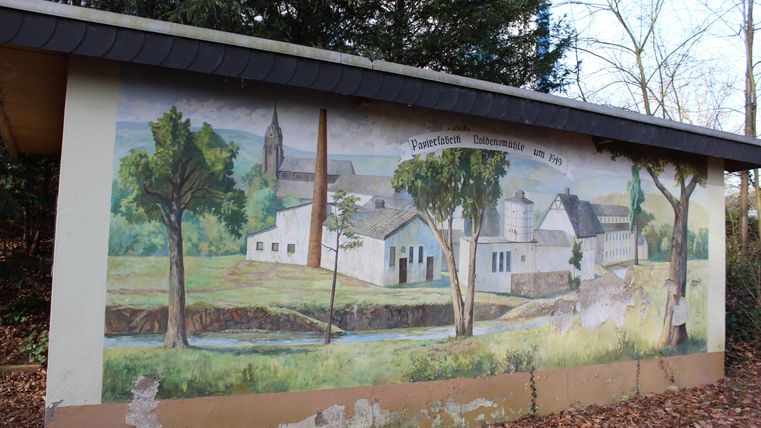A picture of a Noldensmühle mill from 1949 on the outside wall of a small building 