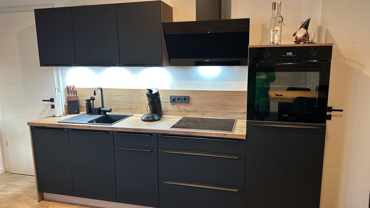 A modern kitchen with black cabinets and wooden surfaces. It is equipped with a stove, sink, and an oven.