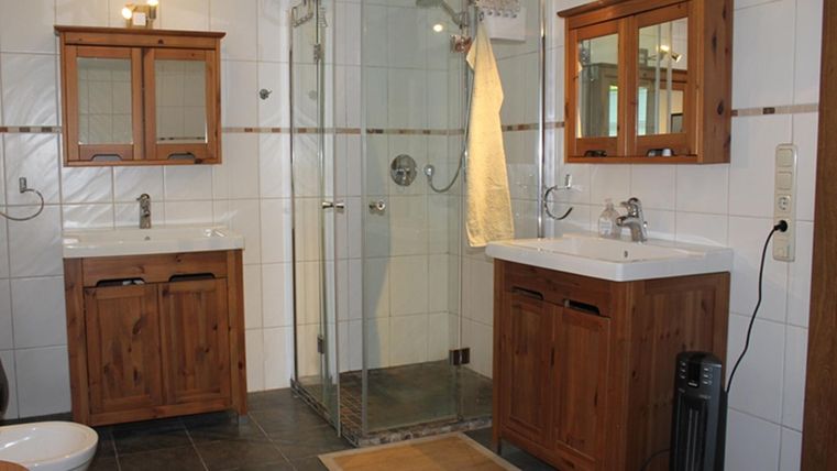 Een moderne badkamer met houten kasten en een douchecabine. De vloer is betegeld met donkere tegels en een tapijt zorgt voor extra comfort.