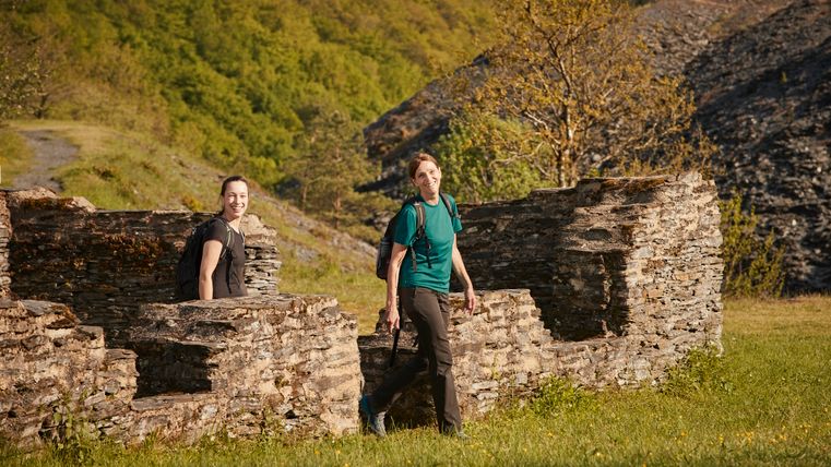 Zwei Personen die zwischen Ruinen aus Bruchstein wandern. 