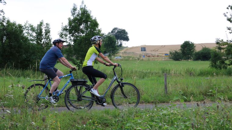 Twee mensen fietsen op een pad door een groen landschap.