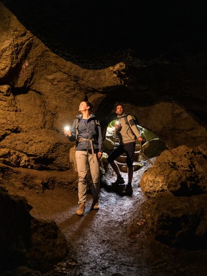 Deux personnes entrent dans une grotte sombre. Tous deux s'éclairent avec les lampes de poche de leurs téléphones portables. Les parois rocheuses de la grotte entourent les randonneurs.