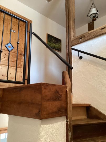 Eine Treppe aus Holz mit einem schönen Geländer und einer Wandart. Im Hintergrund ist eine Tür mit einem dekorativen Gitter zu sehen.