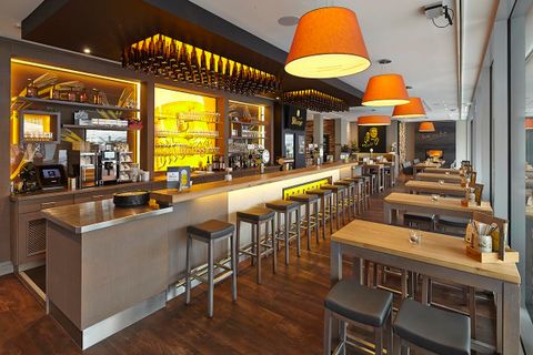 A modern building with glass facades and several commercial units. Outside, there are tables and plants that create an inviting atmosphere.