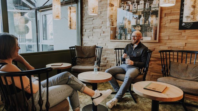 Twee personen zitten ontspannen in een gezellige ginotheek. De inrichting is modern met hout- en lichtelementen.