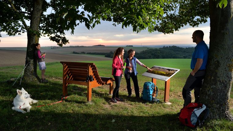Zwei Frauen stehen neben einer Holzliege und schauen auf die Aussichtstafel bei Forst.