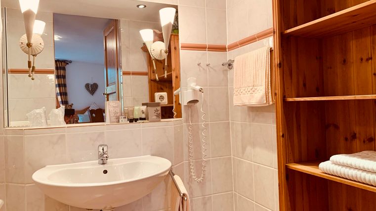 Een modern badkamer met een wastafel, een spiegel en houten planken. Handdoeken en toiletartikelen zijn netjes opgeborgen.