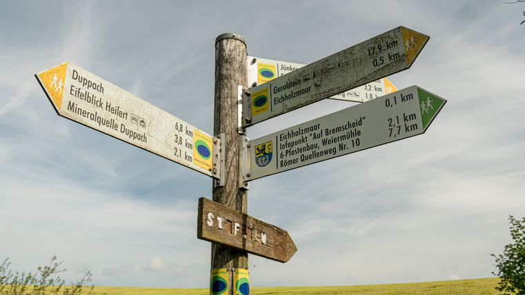 Ein Holzpfahl, an dem mehrere Richtungspfeile angebracht sind und über Wanderwege und Sehenwürdigkeiten in der Umgebung informieren.