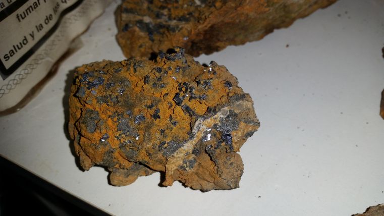 A piece of rock with an orange surface and small sparkling minerals. The texture is rough and irregular.
