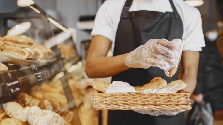 A baker with an apron and gloves is placing fresh pastries in a basket in a bakery.