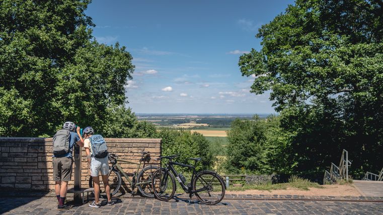 Zwei Radfahrer mit Helmen betrachten die Landschaft von einem Aussichtspunkt in der Eifel.