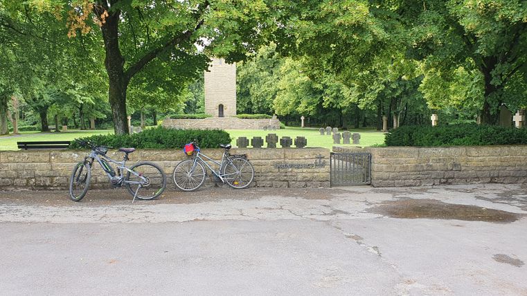 Deux vélos devant un mur de pierre avec un cimetière en arrière-plan.