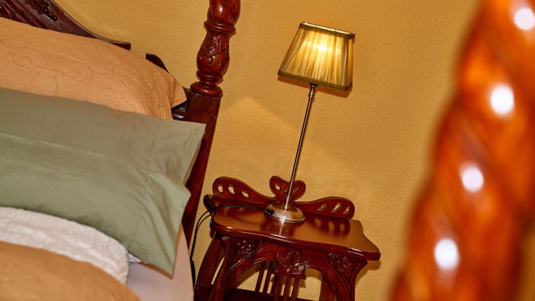 Ein gemütliches Schlafzimmer mit einem großen Bett und eleganter Bettwäsche. Neben dem Bett steht ein Holznachtisch mit einer kleinen Lampe.