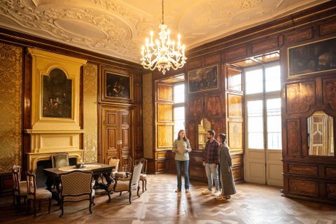 Une chambre élégante avec des murs en bois et un grand lustre. Trois personnes se tiennent à la table et regardent la décoration.