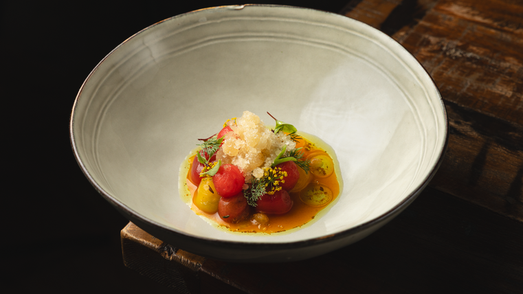 Un plat élégant dans un bol blanc, richement garni de tomates colorées et d'herbes. Au-dessus se trouve une couche de glace qui donne de la fraîcheur au plat.