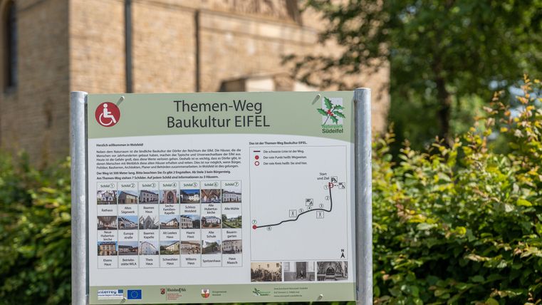 Informationsschild des Themenwegs Baukultur Eifel in Wolsfeld mit Karte und Text.