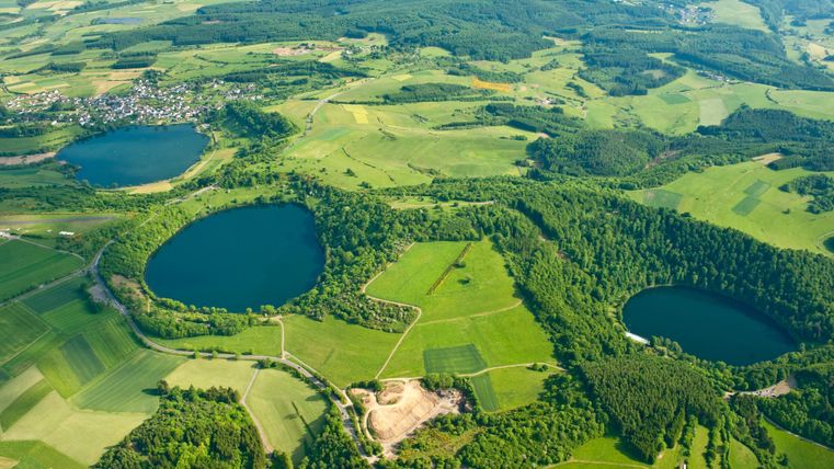Een uitgestrekt landschap met groene velden en twee blauwe meren. De omgeving is heuvelachtig en rijk aan bomen.
