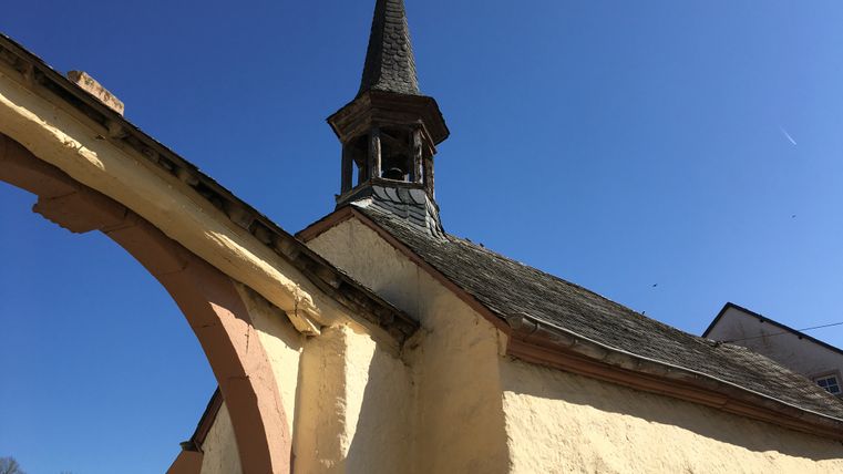 Kapelle in Birtlingen mit spitzem Turm und blauem Himmel.