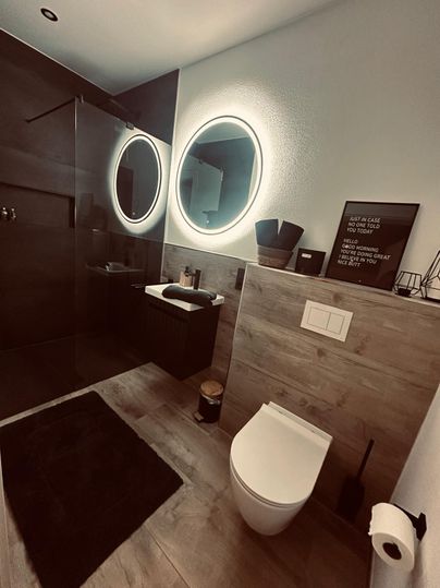 Ein modernes Badezimmer mit einer Dusche und runden Spiegeln. Die Wände sind in dunklen Tönen gehalten, und der Boden ist aus Holz.