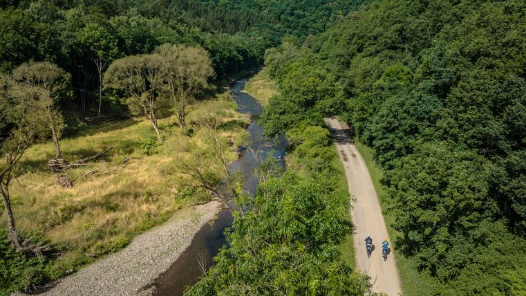 Twee fietsers op een pad naast een rivier in een groen boslandschap.